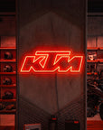 Néon LED mural logo KTM allumé dans un magasin moto, déco garage motard