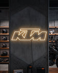 Néon LED mural logo KTM allumé dans un magasin moto, déco garage motard