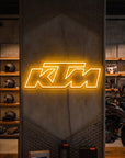 Néon LED mural logo KTM allumé dans un magasin moto, déco garage motard