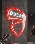 Néon LED mural logo Ducati allumé dans un garage moto, déco motard italien
